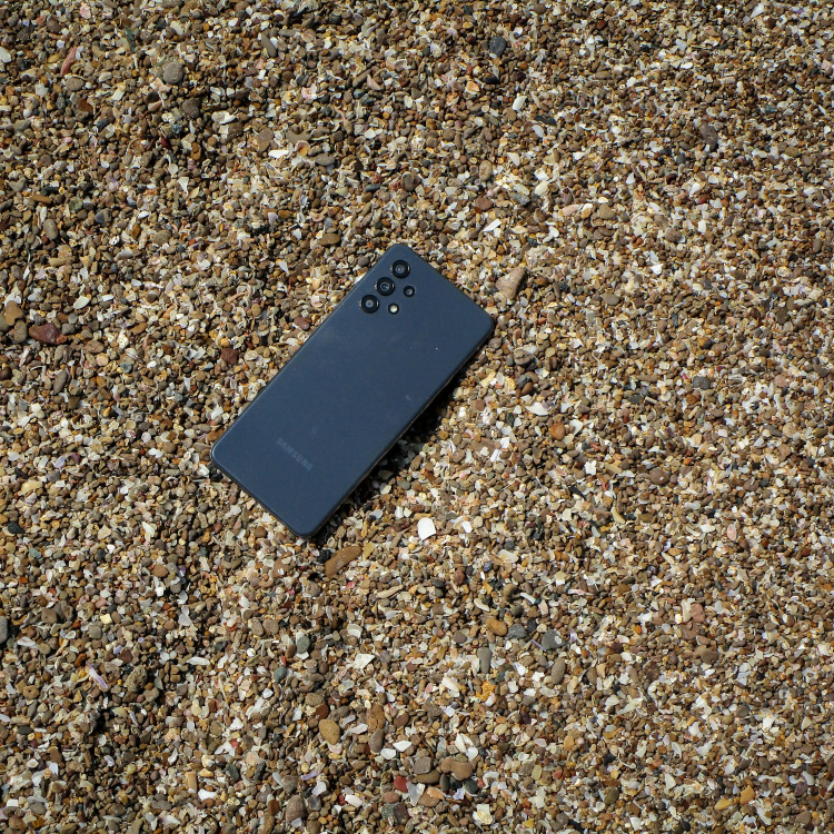 A cell phone laying on the ground covered in sand