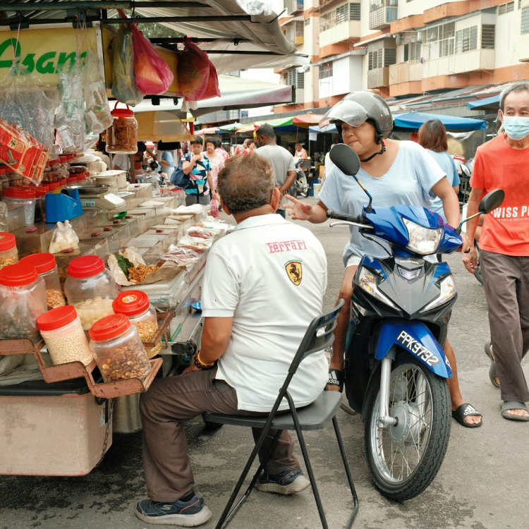 A man sitting on a motorcycle with a cart full of food