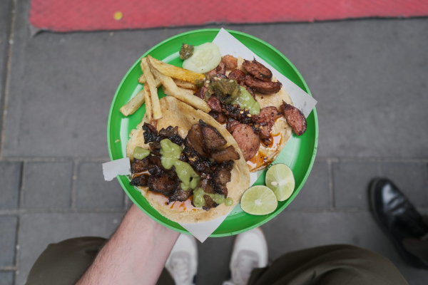 A person holding a plate of food on a sidewalk