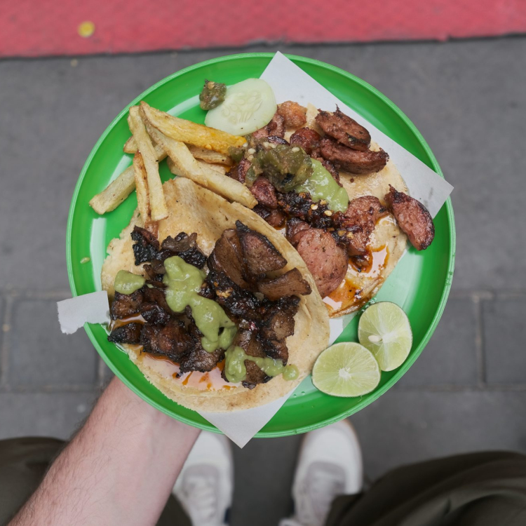A person holding a plate of food on a sidewalk