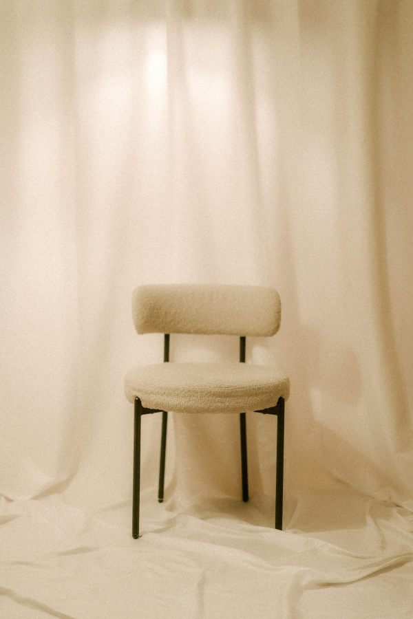 A single chair sits in front of white curtains