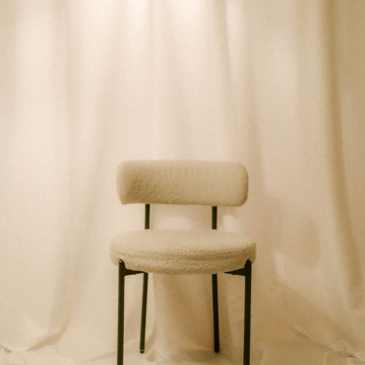 A single chair sits in front of white curtains