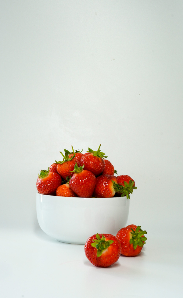 A white bowl filled with lots of ripe strawberries