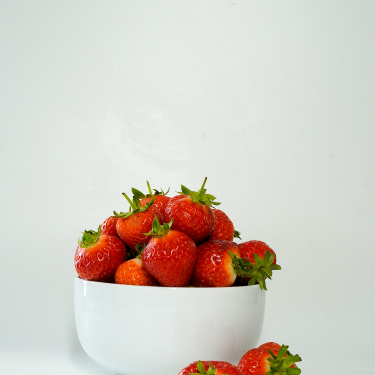 A white bowl filled with lots of ripe strawberries