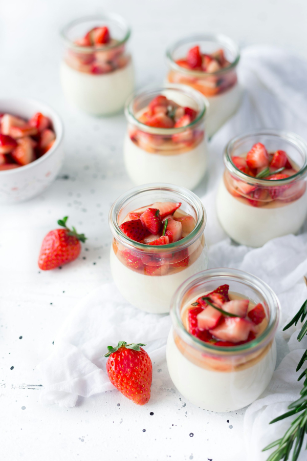 Sliced strawberries in clear glass jar with cream