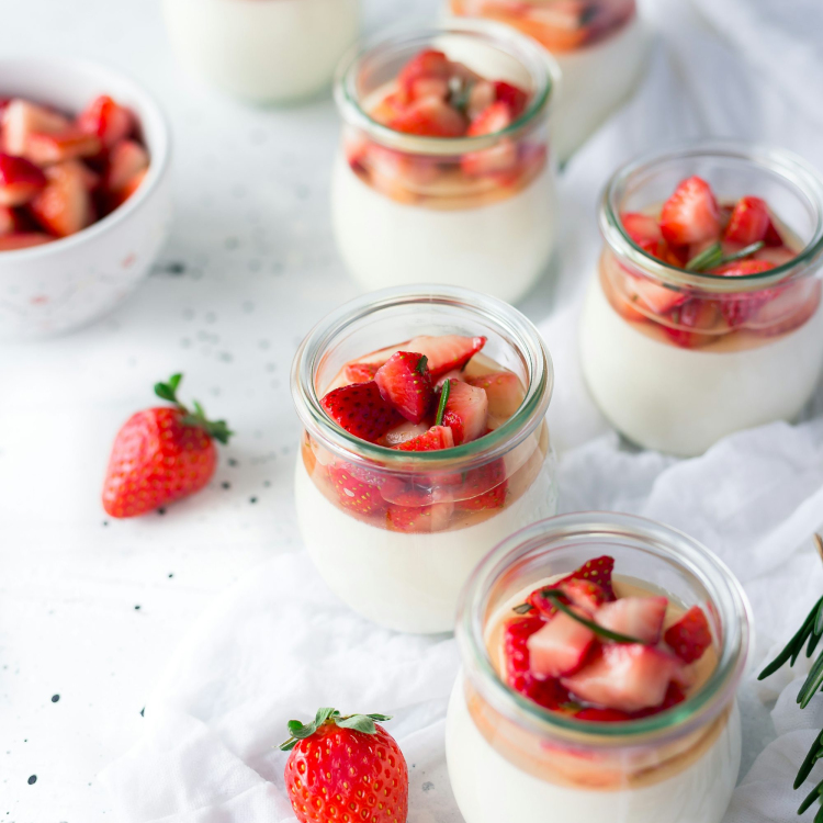 Sliced strawberries in clear glass jar with cream